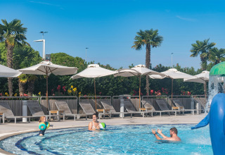 Familie nyder en solrig dag ved poolen med parasoller og palmer på Sandaya Europa Village i Veneto, Italien.