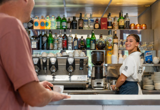 Barkeeperin lächelt Gast an der Bar im Sandaya Europa Village Ferienpark in Venetien, Italien, an.