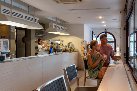Pareja tomando café en un bar moderno mientras camarera sirve una bebida, Sandaya Europa Village, Véneto, Italia.
