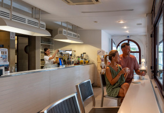 Couple enjoying coffee at a modern bar while bartender pours a drink, Sandaya Europa Village, Veneto, Italy.