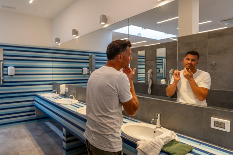 Homme en t-shirt blanc devant le miroir de la salle de bains à Sandaya Europa Village, Vénétie, Italie.