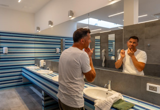 Hombre con camiseta blanca mirando al espejo en el baño de Sandaya Europa Village, Véneto, Italia.