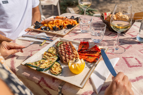 Dos personas cenando pescado a la parrilla, verduras y vino en Sandaya Europa Village, Véneto, Italia.