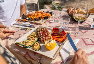 To personer nyder grillet fisk, grøntsager og vin på et udendørs bord på Sandaya Europa Village i Veneto.