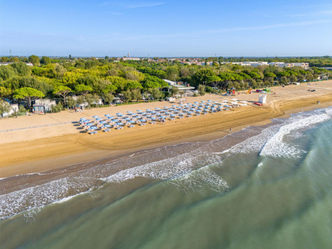 Luftfoto af Sandaya Europa Village ferieparkens strand i Veneto, Italien, med parasoller og grøn skov.