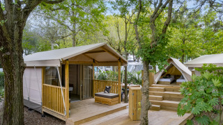 Buitenaanzicht van een safaritent Lodge met houten terras, zitplek en omgeven door groene bomen.