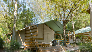 Safari tent Lodge Country in de natuur, met houten veranda en zithoek onder groene bomen.