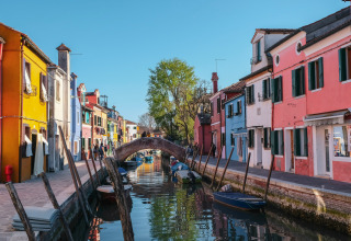 Casas coloridas junto a un canal cerca de Cavallino Treporti, Véneto, Italia, con botes y un puente de piedra.