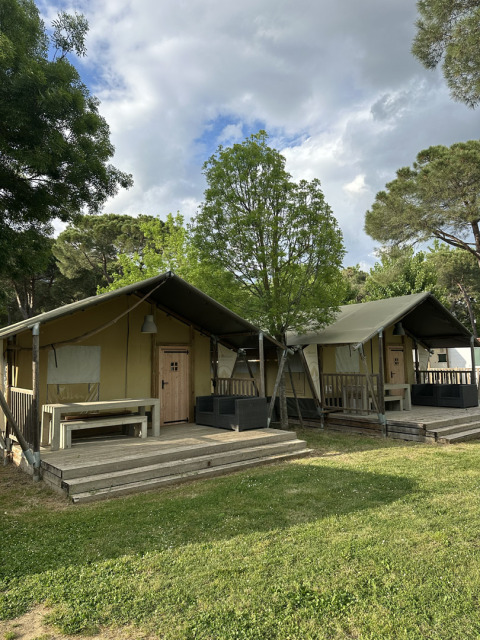 Twee Villatent Nomad safaritenten op Camping Punta Navaccia in Italië, omgeven door bomen en gras.