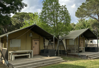Due tende safari Villatent Nomad al Camping Punta Navaccia, Italia, circondate da alberi e prato verde.
