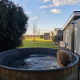 Persoon ontspant in een buitenjacuzzi bij lodge Ravenbosch op Resort Mooi Bemelen, Nederland, zonnige dag.