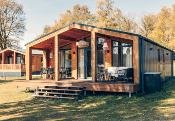 Modern houten huisje The Beach House met ruim terras en buitenzitjes op een zonnige dag in de natuur.
