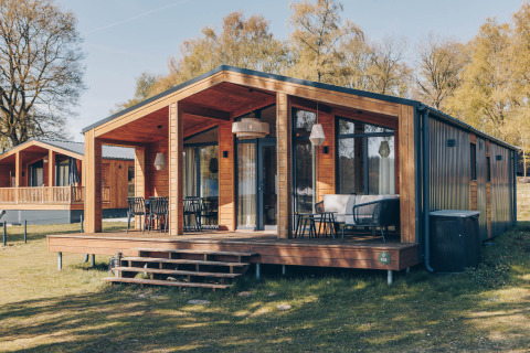 Modernes Holzhaus mit großer Terrasse und Sitzgelegenheiten im Freien an der Beach House Lodge am Tag.