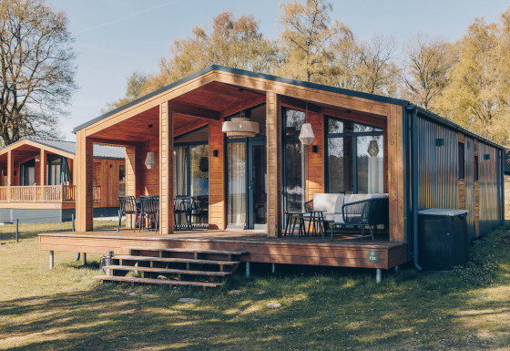 Modernes Holzhaus mit großer Terrasse und Sitzgelegenheiten im Freien an der Beach House Lodge am Tag.