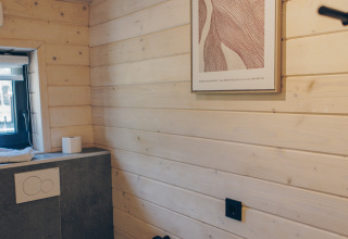 Modernes Badezimmer mit Holzverkleidung, Wandtoilette und Kunstwerk im The Beach House in Wilsumer Berge, Deutschland.
