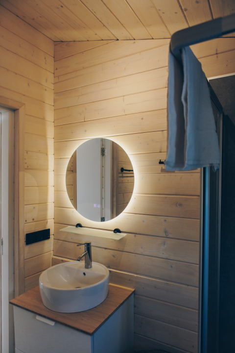 Salle de bain moderne au Beach House à Wilsumer Berge avec miroir rond et murs en bois clair.