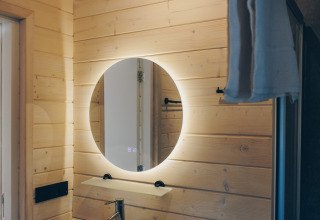 Salle de bain moderne au Beach House à Wilsumer Berge avec miroir rond et murs en bois clair.