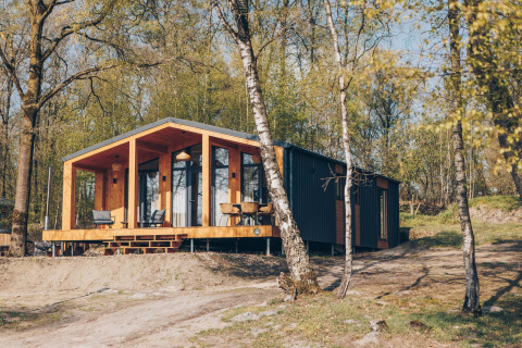 Moderne Hill Side Scandi lodge met hot tub, omgeven door bomen en natuur, buitenaanzicht.