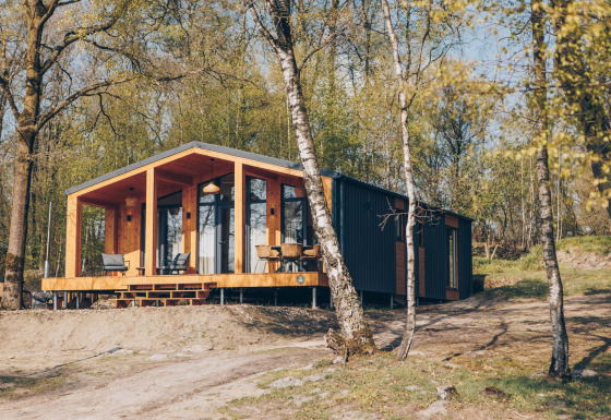 Moderne Hill Side Scandi lodge met hot tub, omgeven door bomen en natuur, buitenaanzicht.