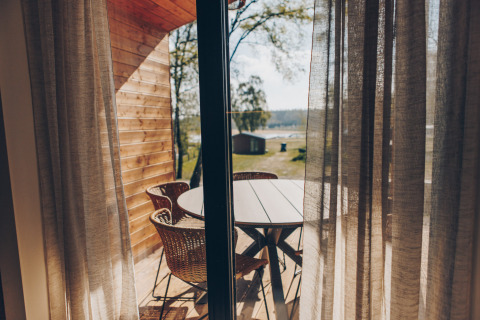 Uitzicht door gordijnen op terras met rotan stoelen en tafel bij Hill Side Scandi, Wilsumer Berge, Duitsland.