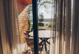 Uitzicht door gordijnen op terras met rotan stoelen en tafel bij Hill Side Scandi, Wilsumer Berge, Duitsland.