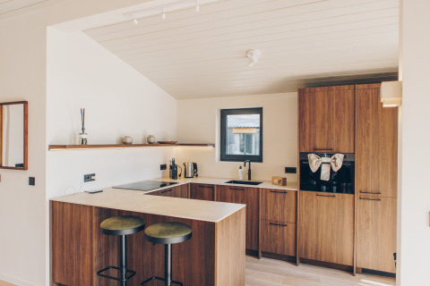 Moderne houten keuken in de Hill Side Scandi lodge op Wilsumer Berge, Duitsland, met bar en stoelen.