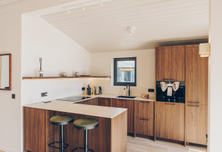 Moderne houten keuken in de Hill Side Scandi lodge op Wilsumer Berge, Duitsland, met bar en stoelen.