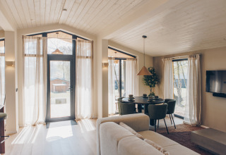 Lichte woonruimte in de Hill Side Scandi lodge bij Wilsumer Berge, Duitsland, met grote ramen en eethoek.