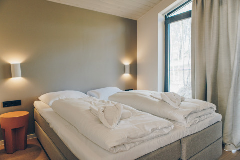 Modern bed met witte dekbedden en handdoekharten bij Hill Side Scandi, Wilsumer Berge, Duitsland.