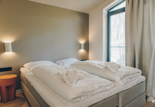 Modern bed met witte dekbedden en handdoekharten bij Hill Side Scandi, Wilsumer Berge, Duitsland.