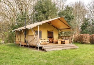 Safari-Zelt mit überdachter Terrasse und Sitzgelegenheiten, umgeben von Bäumen und grünem Rasen.