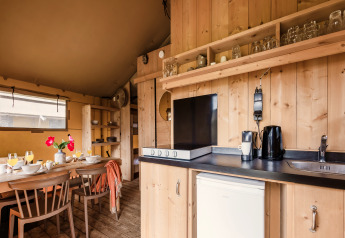 Cucina moderna e zona pranzo in una tenda safari, con finiture in legno, stoviglie e utensili.