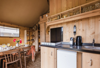 Cuisine moderne et coin repas dans une tente safari, avec mobilier en bois, vaisselle et ustensiles.