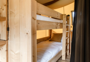 Interno di una tenda safari con letto a castello in legno, biancheria bianca e pavimento in legno per glamping.