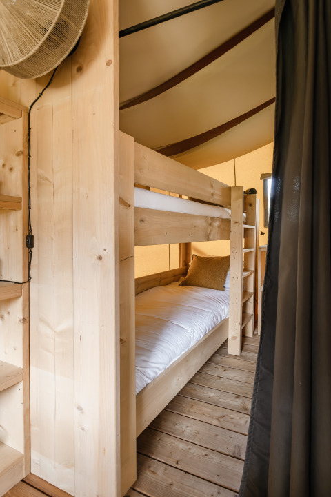 Intérieur d'une tente safari avec lit superposé en bois, draps blancs et plancher en bois pour le glamping.