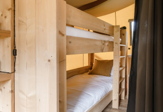 Intérieur d'une tente safari avec lit superposé en bois, draps blancs et plancher en bois pour le glamping.