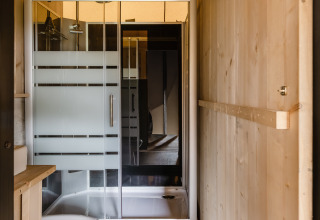 Salle de bain dans une tente safari avec murs en bois, douche en verre, toilettes et sol stratifié.