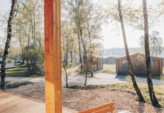 View from Beach Side Scandi lodge at Wilsumer Berge, showing trees, paths, and modern cabins in Germany.
