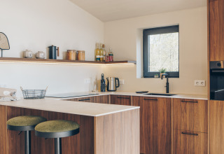Modern kitchen at Beach Side Scandi in Wilsumer Berge, Germany featuring wood cabinets and green stools.