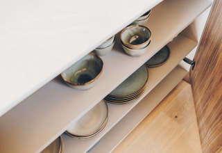 Ceramic bowls and plates neatly stored in the kitchen cupboard at Beach Side Scandi Lodge, Wilsumer Berge.