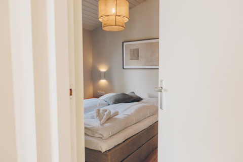A peek into a cozy bedroom with a double bed, soft lighting, and modern Scandinavian decor style.