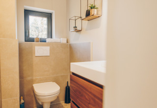 Modern bathroom with wall-mounted toilet, wooden vanity, small window and shelves at Beach Side Scandi lodge.