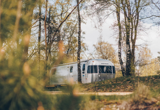 Airstream tiny house met bubbelbad, omgeven door bomen in een vredig bosgebied.