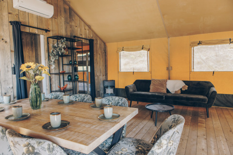 Interieur van een safaritent met houten muren, eettafel, gezellige zetel en bloemen in een vaas.
