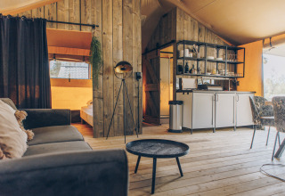Interieur van een ruime safaritent met houten wanden, bank, keukenblok en eethoek.