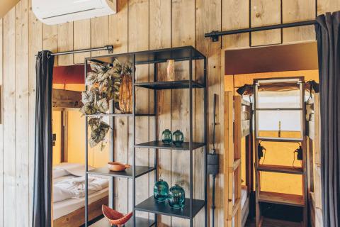 Interieur van een safaritent met houten panelen, stapelbedden en moderne decoratie op de rekken.