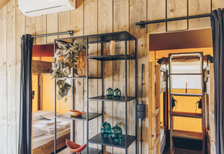 Interieur van een safaritent met houten panelen, stapelbedden en moderne decoratie op de rekken.