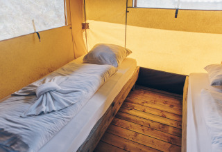 Binnenzicht van een safaritent met twee eenpersoonsbedden, houten vloer en warm binnenvallend licht.
