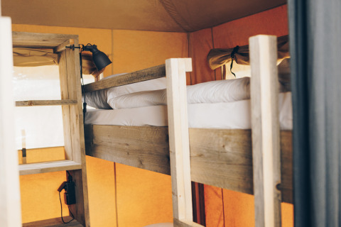 Houten stapelbed met witte lakens in een safaritent met oranje muren en zacht natuurlijk licht.