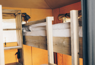 Houten stapelbed met wit beddengoed in een safaritent met oranje wanden en zacht daglicht.